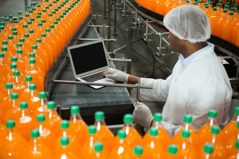 Quality technician with a laptop monitoring a juice bottling line